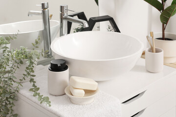 Soap bars, dispenser, houseplant and sink bowl on chest of drawers in bathroom