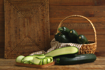 Wicker basket with many fresh zucchini and board of slices on wooden background