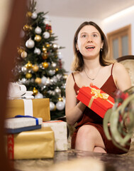 Happy young woman prepares Christmas presents at home for guests, being in anticipation of the...