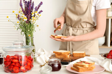 Woman preparing tasty toasts with sweet strawberry jam at table in kitchen