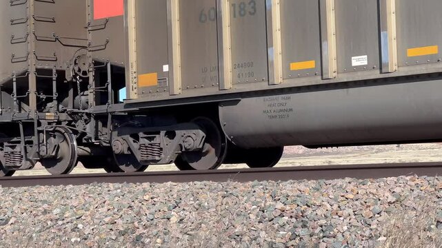 A freight train moves across the desert seen from a low angle, pan focused on wheels while turning left to right