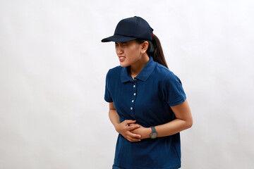 Young asian woman courier wearing delivery uniform and cap with hand on stomach because nausea, painful disease feeling unwell. ache concept.