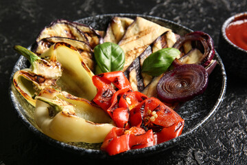 Plate with tasty grilled vegetables on black background