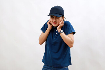 Young asian woman courier wearing delivery uniform and cap covering ears with fingers with annoyed expression for the noise of loud music. deaf concept.