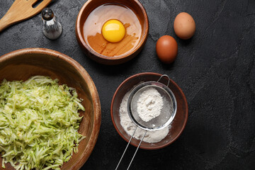Bowls with ingredients for preparing zucchini fritters on black background