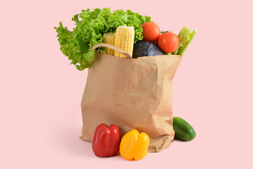 Paper bag with fresh vegetables on pink background. Grocery shopping concept