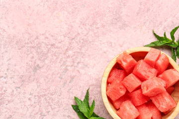 Bowl with pieces of fresh watermelon and mint on pink background