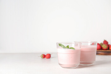 Glasses of tasty strawberry smoothie on light background