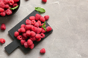 Board and bowl with fresh raspberries on grey table