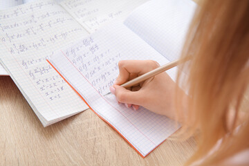 Woman writing math formulas in copybook on wooden table