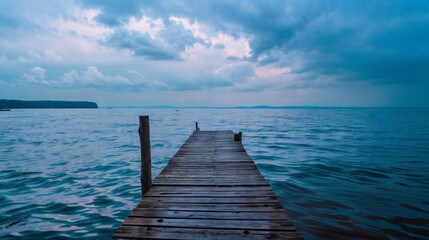 Fototapeta premium A wooden pier stretching into a calm lake under a cloudy sky at dusk, evoking a peaceful and reflective mood..