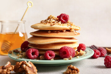 Plate of tasty pancakes with raspberries on light background