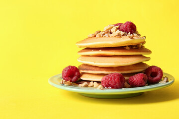 Plate of tasty pancakes with raspberries on yellow background