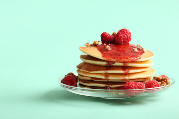 Plate of tasty pancakes with raspberries and nuts on turquoise background