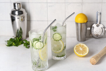Glasses of mojito with cucumber and pestle on grunge white table