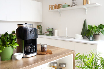 Modern coffee machine with jar of beans and cup on wooden table in kitchen