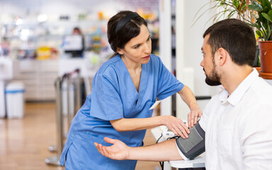 Nurce measuring man's blood pressure in drugstore. Diagnostic procedure in pharmacy.