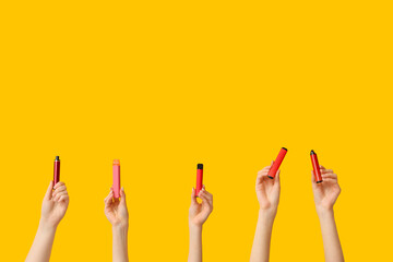 Many hands holding electronic cigarettes on yellow background