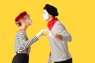 Couple of pantomimists making heart with their hands on yellow background