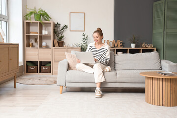 Obraz premium Young woman using modern laptop on sofa at home