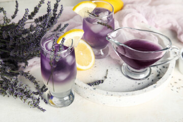 Board with glasses of cold lavender lemonade, flowers and syrup on light background