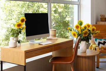 Beautiful workplace with computer and sunflowers in interior of cozy room