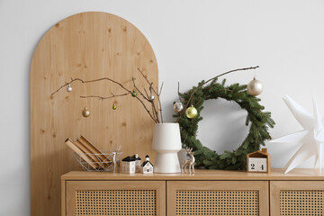 Vase with tree branches, Christmas balls and wreath on commode in room