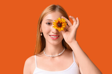 Beautiful young happy woman in stylish outfit with flower on orange background