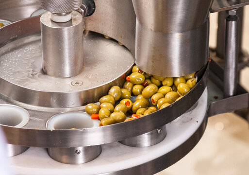 Automated machine filling olives with pimentos into containers.
