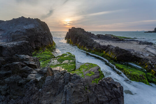 Sunset over mossy rocks and vibrant sea creating contrast