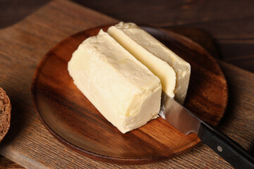 Plate with fresh butter and knife on wooden board, closeup