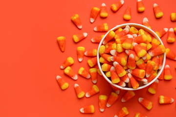 Bowl of tasty Halloween candy corns on orange background