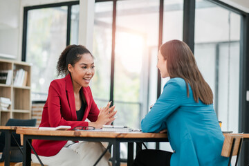 Two professional women engaged in a business meeting in a modern office with large windows and natural light.