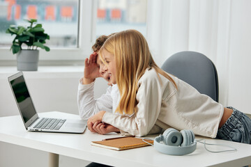 Happy Caucasian children studying online with laptops at home, sitting at a table in the living room The boy and girl are engrossed in their elearning lessons, wearing headphones and typing on their