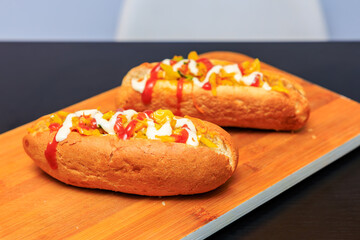 Two hot dogs with ketchup and mustard on a wooden cutting board