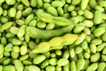 Raw green edamame pods on soybeans as background, top view