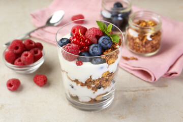 Tasty yogurt with fresh berries, granola and mint in glass on gray textured table, closeup