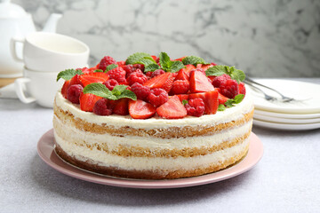 Tasty sponge cake with fresh berries and mint on light gray table