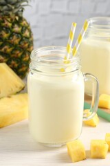 Tasty pineapple smoothie in mason jar and fresh fruit on white wooden table