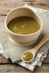 Delicious baby food in bowl with spoon on wooden table