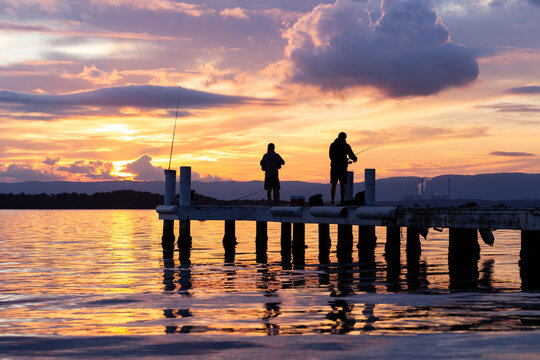 Silhouetted fishermen fishing on jetty at sunset