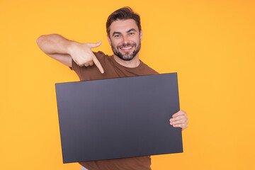 Happy man with blank banner isolated on studio background. Portrait of attractive man with empty blank poster. Man showing poster, pointing finger on signboard placard. Billboard or banner concept.