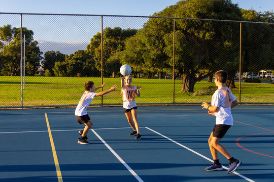 three children doing a netball training drill on blue playing surface outdoors