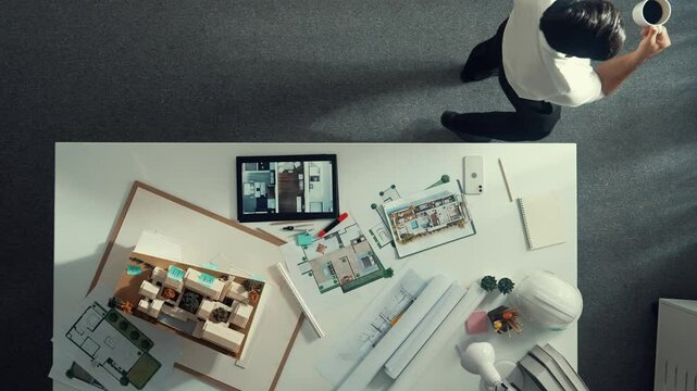 Top view of engineer drink coffee and thinking about house plan at meeting table with equipment and safety helmet scatter around. Aerial view of stressful manager walking and standing. Alimentation.