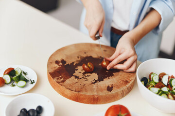 Woman preparing dinner on kitchen table with tomatoes, cutting board, and bowls of food
