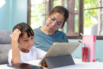 A woman and a child are sitting at a table with a tablet in front of them