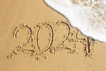 happy new year 2024. number 2024 write on sandy beach with ripple ocean wave splash with white bubble. countdown for happy new year turning from 