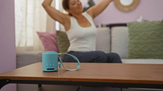 Woman dancing while sitting on a sofa in a living room with a focus on a blue bluetooth speaker on a wooden table