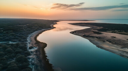 Fototapeta premium The drone captures a tranquil coastal lagoon during sunset, with calm waters reflecting the warm colors of the sky
