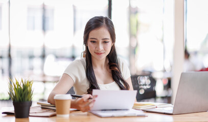 Asian young business woman working on laptop computer reading financial document report in office. Accountant entrepreneur manager businesswoman doing paperwork. Copy space